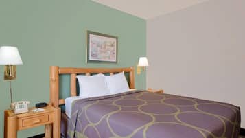 A neatly made bed with a purple and green patterned bedspread, two bedside lamps, a wooden nightstand with a telephone, and a framed picture on the wall.