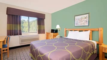A hotel room with a bed, a desk, a chair, a window with curtains, a heater, a lamp, a nightstand, and a painting on the wall.