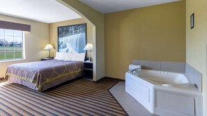 A hotel room with a bed, a large window, a painting, a bathtub, and a nightstand with a lamp. - Super 8 by Wyndham Nixa/Springfield Area (Nixa)