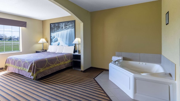 A hotel room with a bed, a large window, a painting, a bathtub, and a nightstand with a lamp. - Super 8 by Wyndham Nixa/Springfield Area (Nixa)