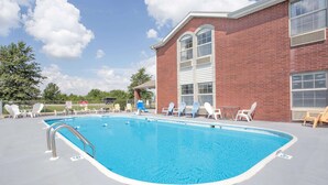 A rectangular pool with a metal ladder, surrounded by white lounge chairs and a brick building with large windows. - Super 8 by Wyndham Nixa/Springfield Area (Nixa)