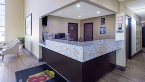 A reception area with a marble counter, a reception desk, a seating area with chairs, a plant, and a wall-mounted security camera. - Super 8 by Wyndham Nixa/Springfield Area (Nixa)