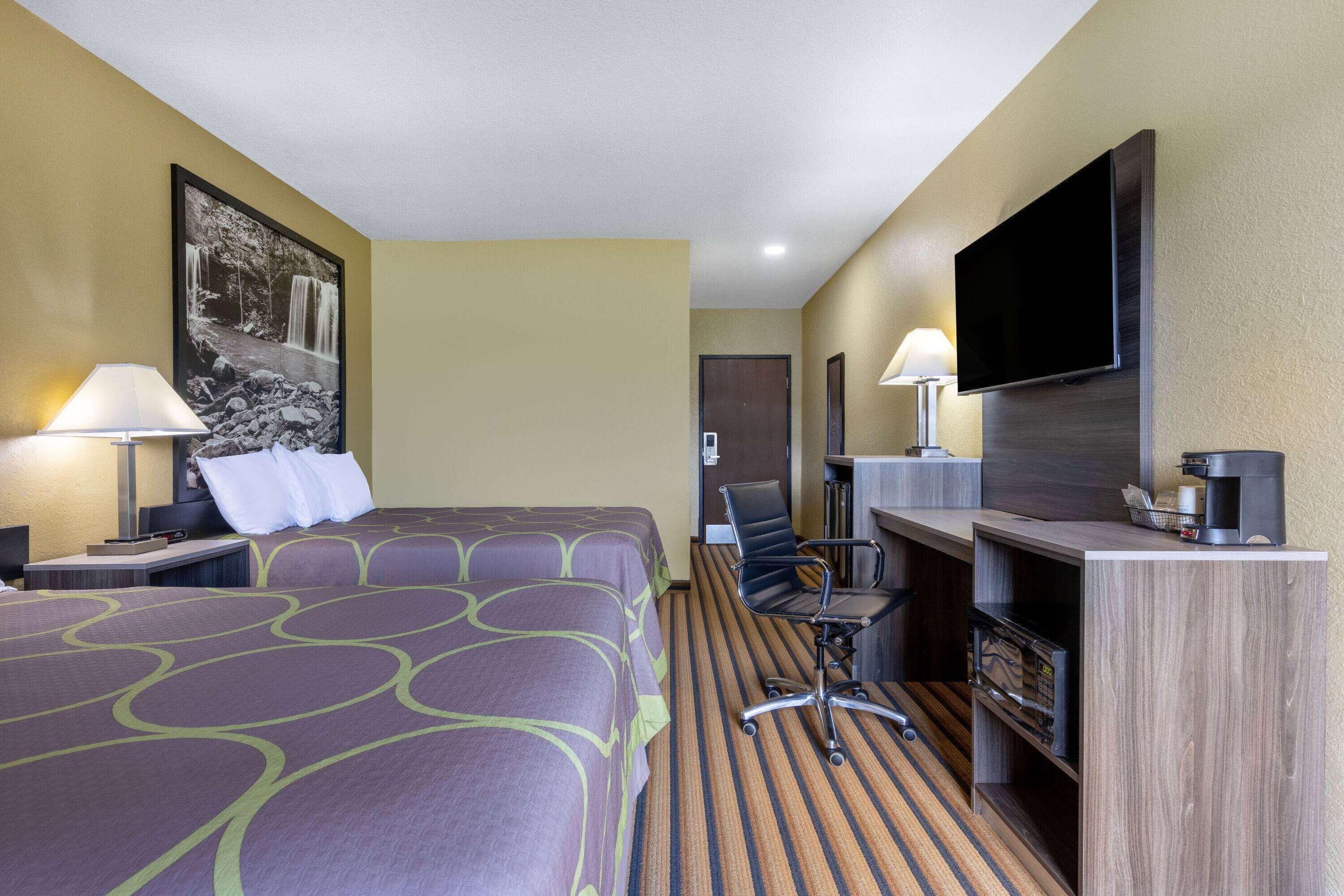 A hotel room with a large bed, two bedside tables with lamps, a desk with a flat-screen TV, a chair, and a coffee machine.