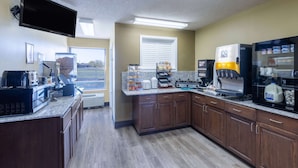 A modern kitchen with granite countertops, a coffee machine, a refrigerator, and a window with blinds. - Super 8 by Wyndham Nixa/Springfield Area (Nixa)