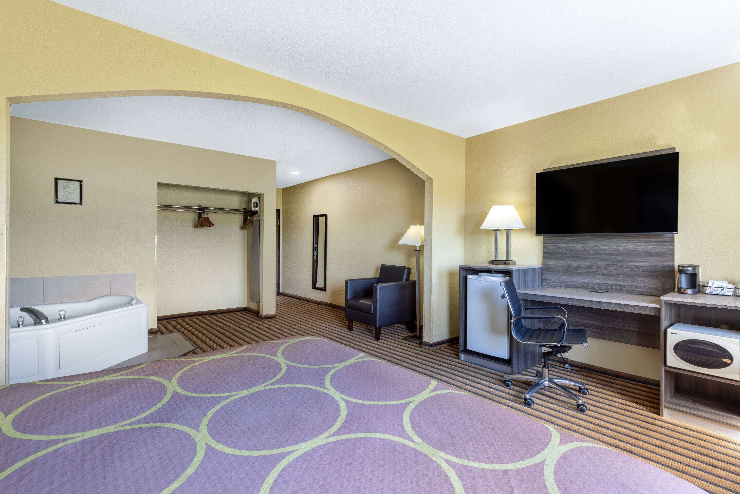 A hotel room with a bed, a desk, a chair, a TV, a desk lamp, and a small refrigerator.