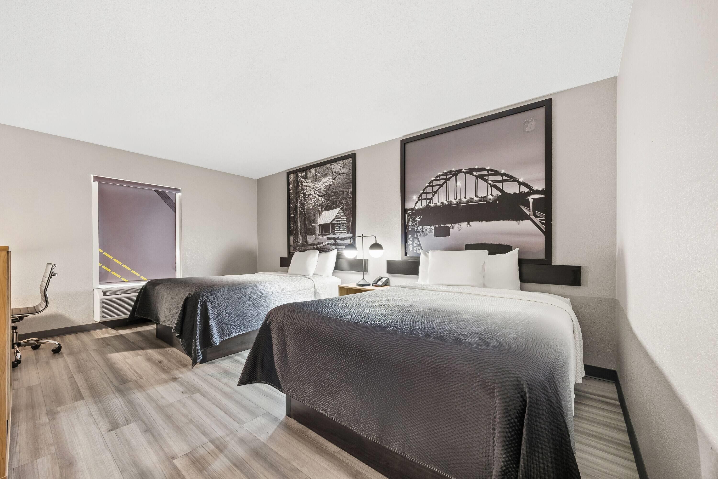 A hotel room with two beds, a desk, a chair, and a window with a view of a bridge.