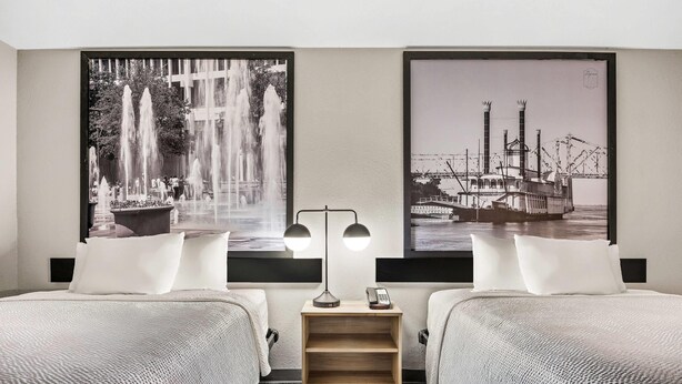 Una habitación de hotel con dos camas, una mesita de noche con una lámpara, y dos fotografías grandes en blanco y negro en las paredes.