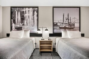 A hotel room with two beds, a nightstand with a lamp, and two large black-and-white photographs on the walls. - Super 8 by Wyndham Harrison AR (Harrison)