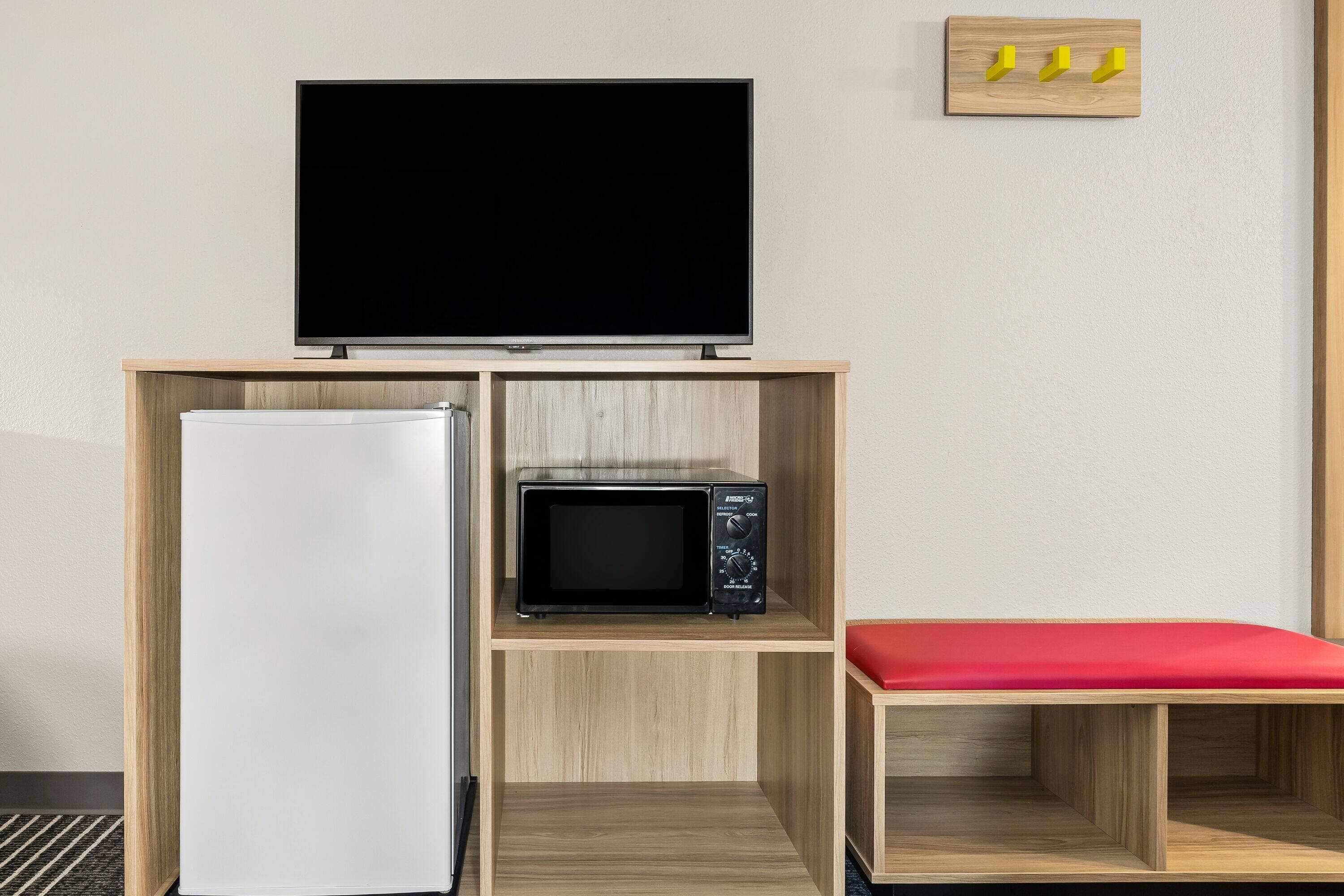 A kitchenette with a refrigerator, microwave, and a flat-screen TV on a wooden shelf.