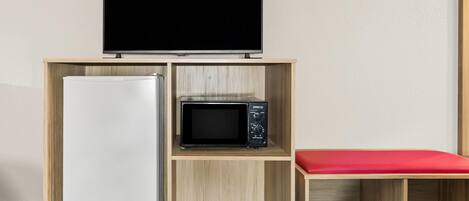 A kitchenette with a refrigerator, microwave, and a flat-screen TV on a wooden shelf.