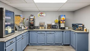 Una cocina con armarios azules, un refrigerador, un microondas, una cafetera y un dispensador de jugo.