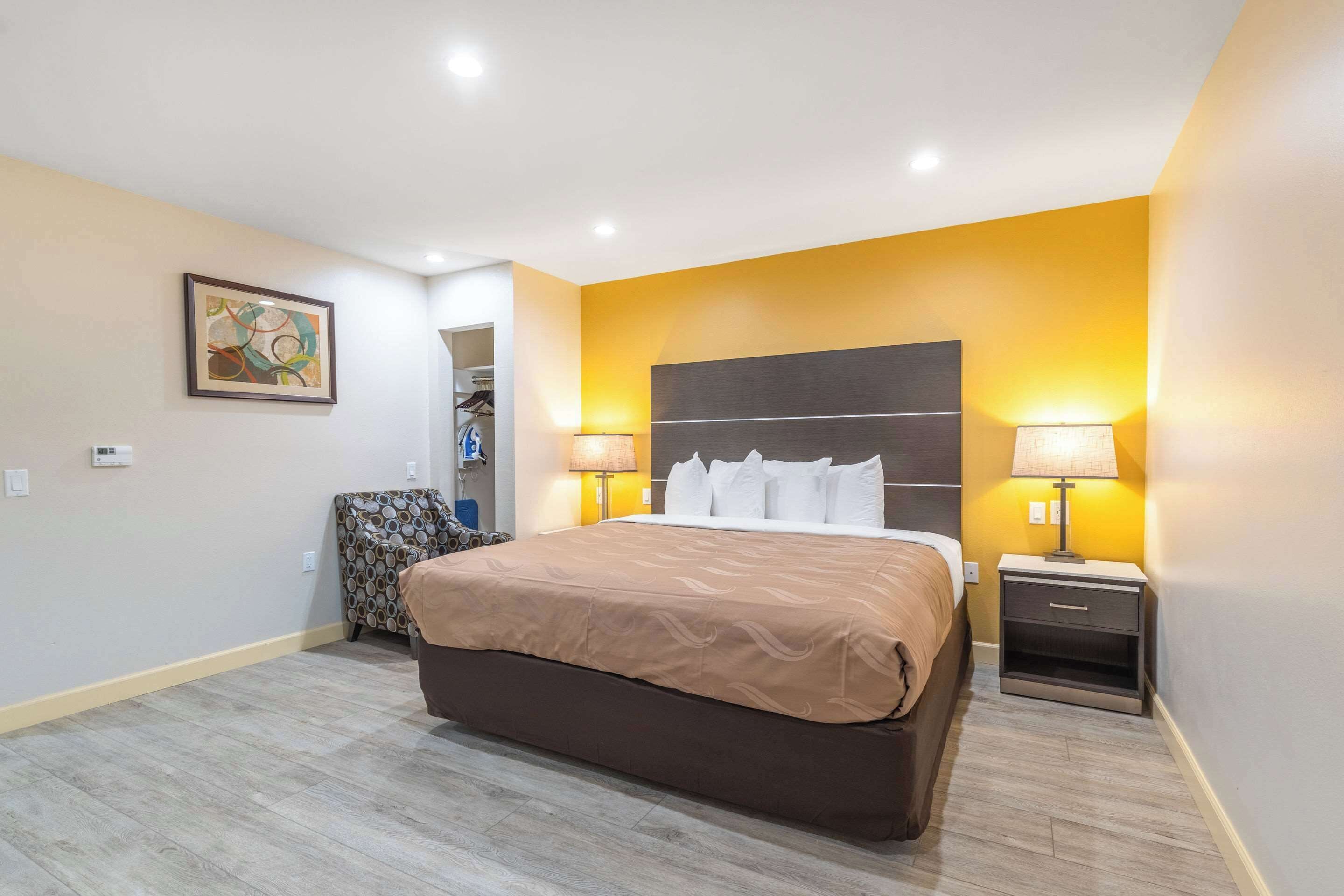 A hotel room with a large bed, two bedside tables with lamps, a wardrobe, and a painting on the wall.