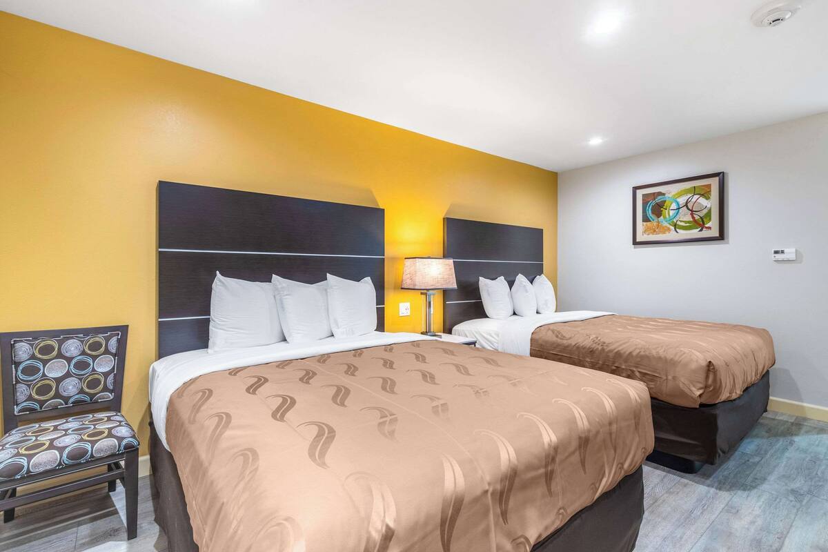 Habitació d'hotel amb dos llits, una cadira, una làmpada i un quadre a la paret.