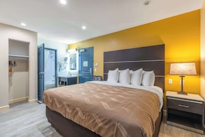 A hotel room with a bed, bedside table, and a bathroom with a shower and mirror.