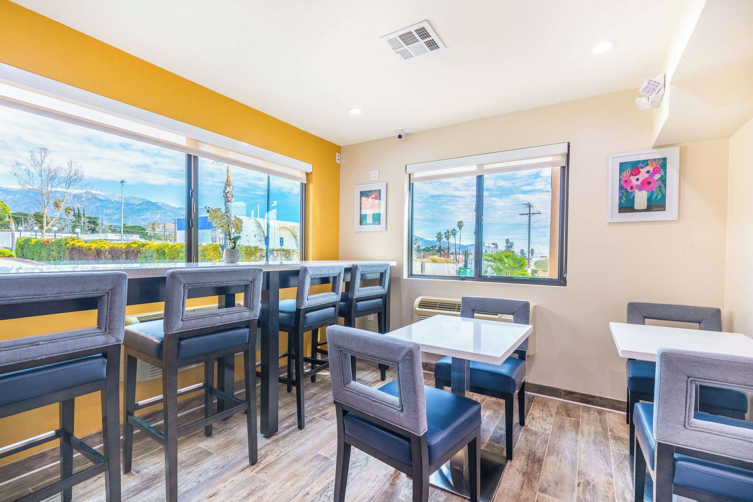 Un área de comedor con mesas y sillas, ventanas amplias con vistas a montañas y vegetación, y obras de arte en las paredes.