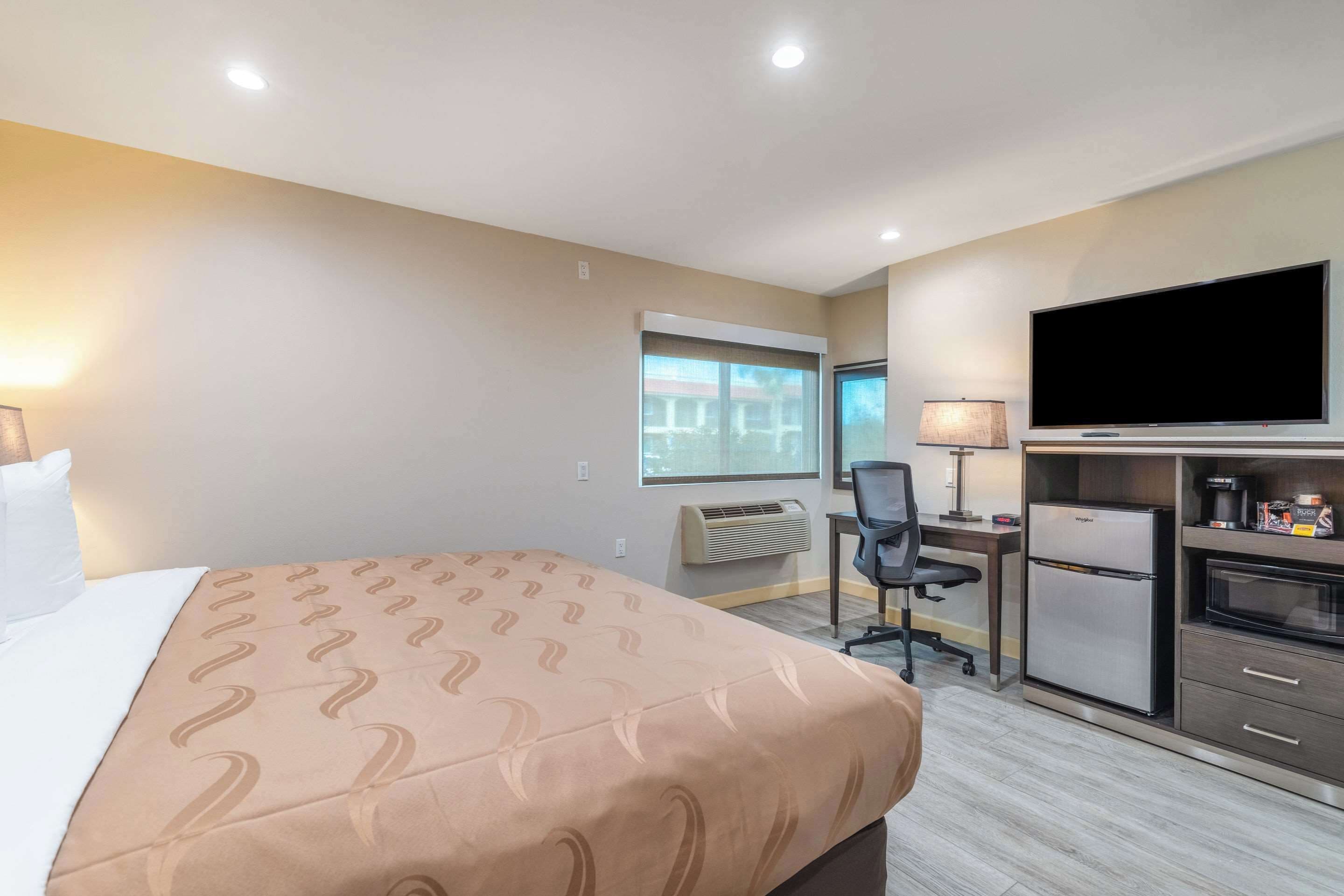 A hotel room with a bed, a desk with a chair, a television, a refrigerator, and a microwave.