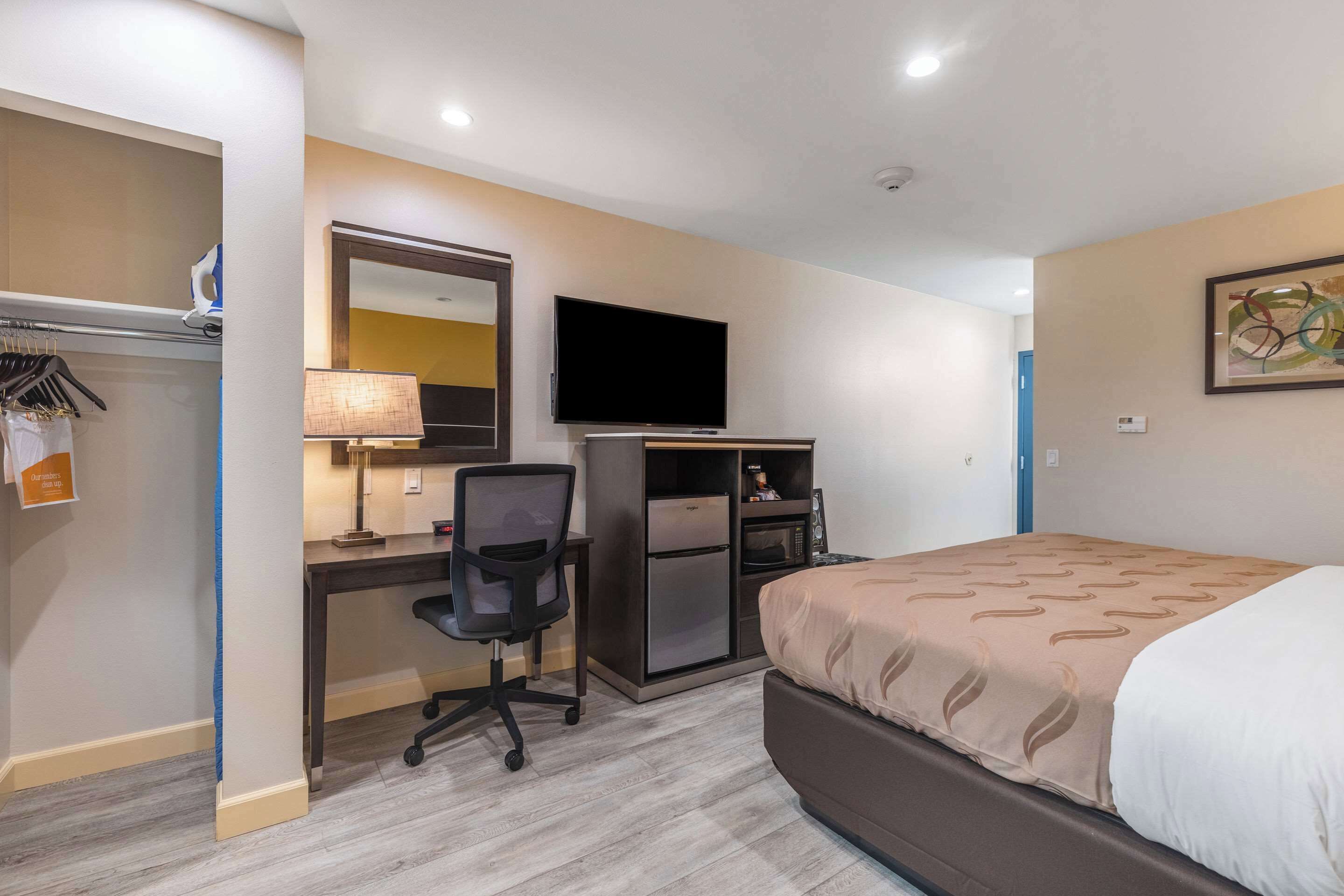 A hotel room with a bed, desk, chair, TV, and a microwave.