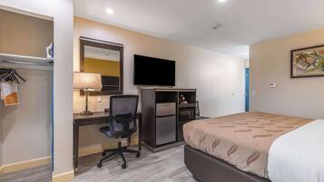 A hotel room with a bed, desk, chair, TV, and a microwave.