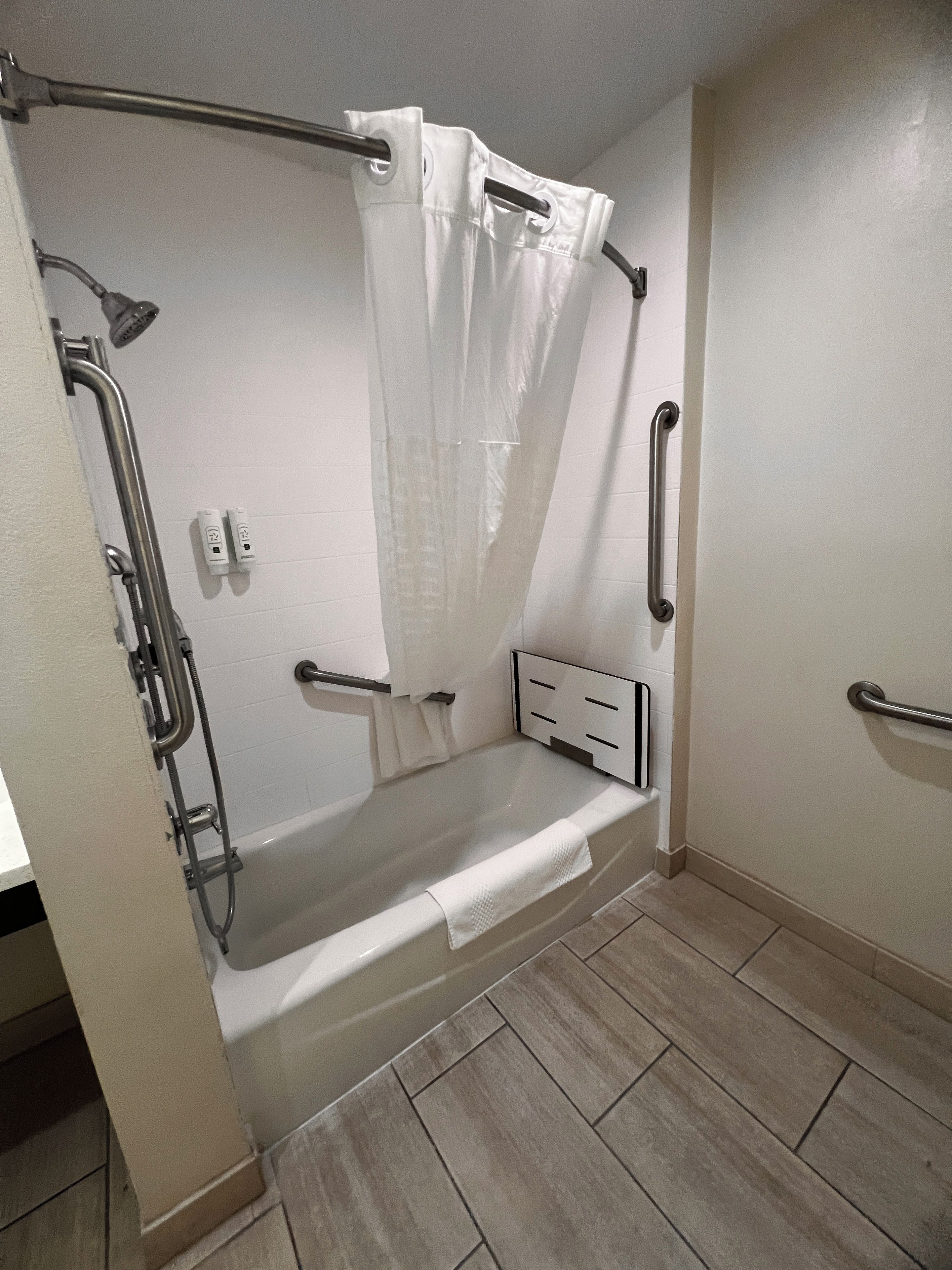 Ein Badezimmer mit begehbarer Dusche, Haltegriffen, einem Handtuchhalter und einer Bedienkonsole.