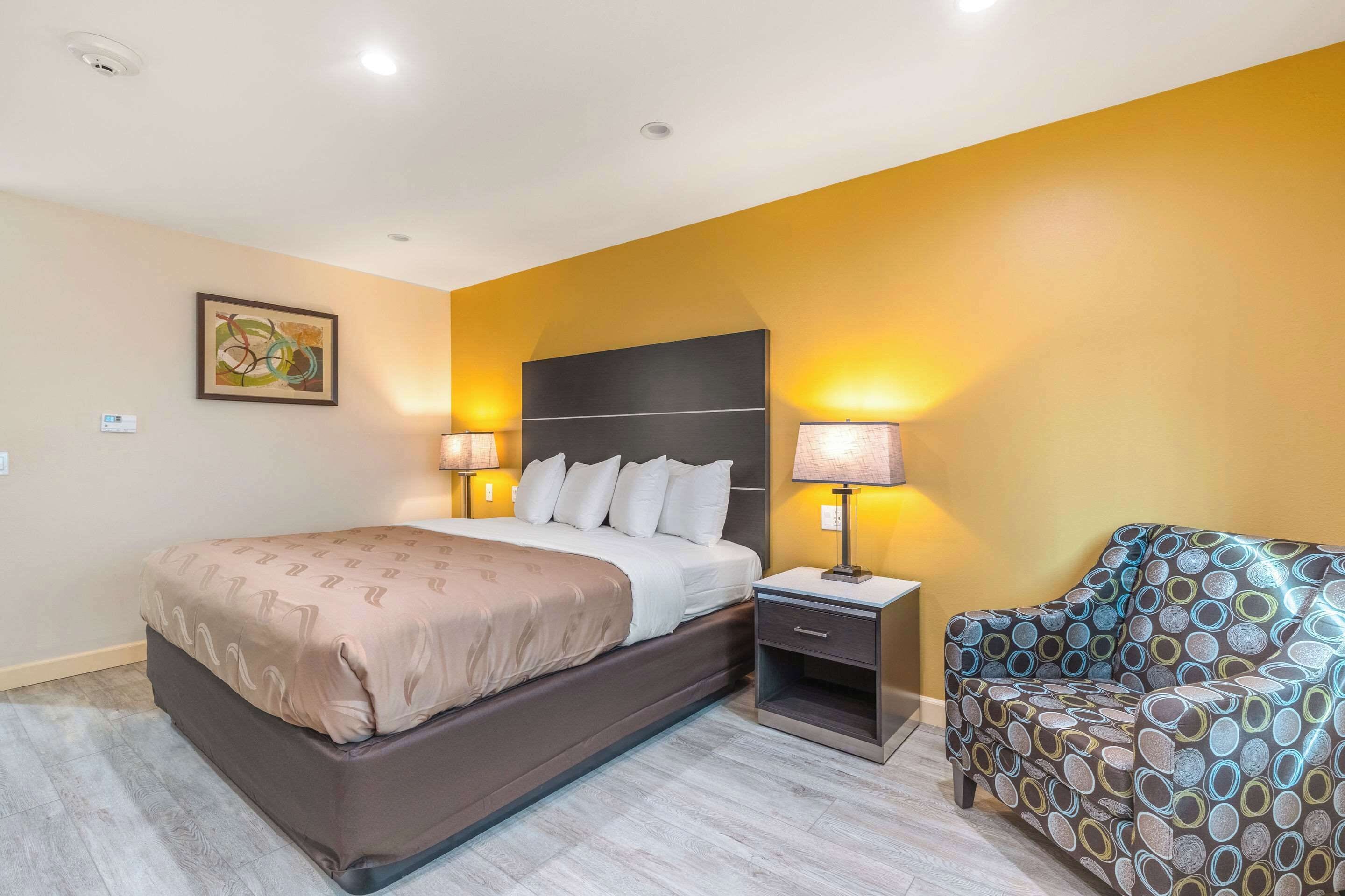 A hotel room with a bed, bedside lamps, a sofa, and a painting on the wall.