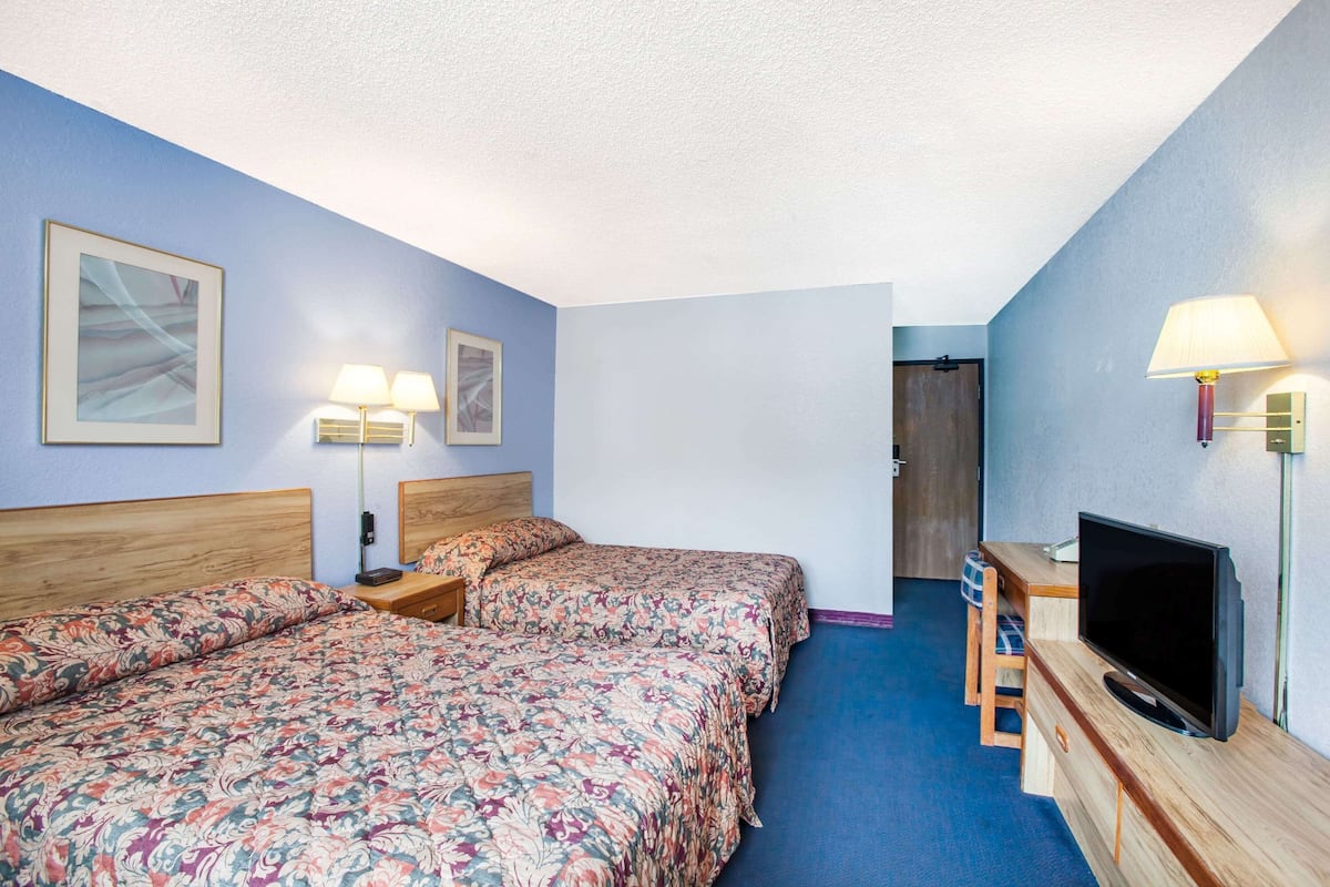 A hotel room with two beds, a TV, and a desk with a chair.