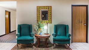 Una habitación con dos sillones azul verdosos, una mesa de madera con un florero y una lámpara, y un espejo con un borde de girasoles.