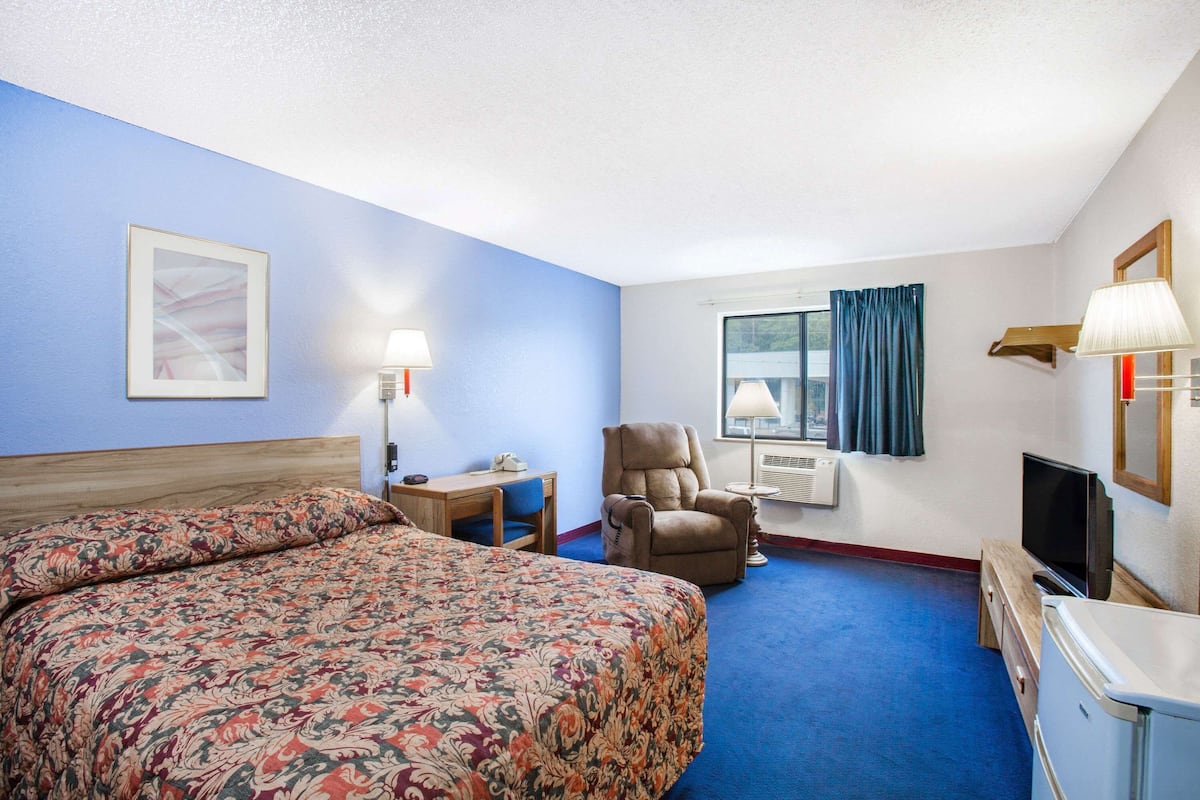 A hotel room with a large bed, a desk with a chair, a television, and a window with curtains.