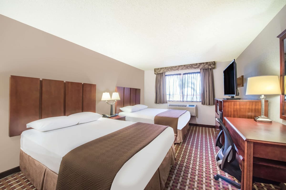 A hotel room with two beds, a desk, a chair, a television, and a window with curtains.