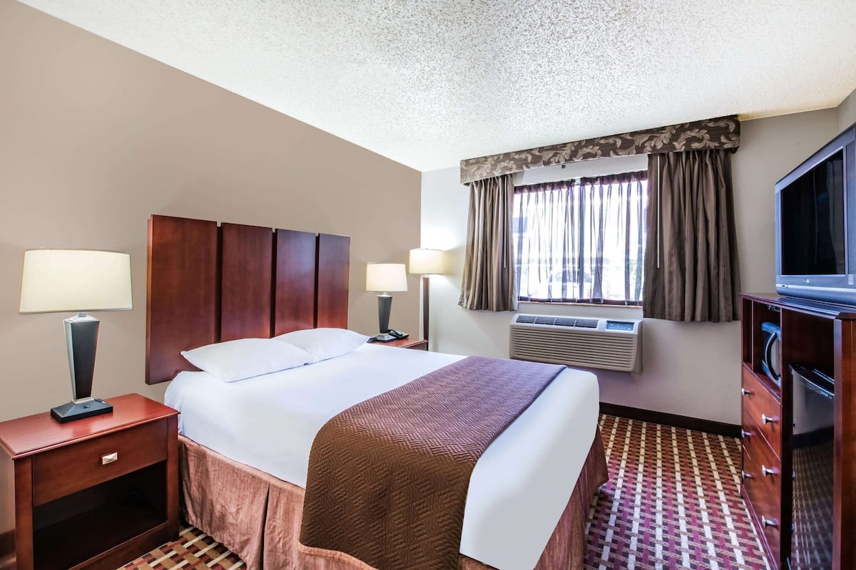 A hotel room with a bed, bedside lamps, a television, a dresser, and an air conditioning unit.