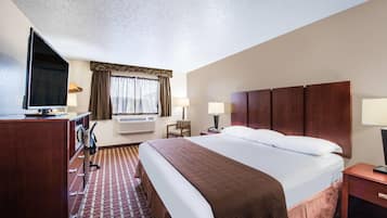 Een hotelkamer met een groot bed, een bureau met een televisie, een stoel, een lamp en een airconditioner.