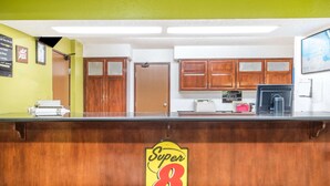 A reception desk with a 'Super 8' sign, wooden cabinets, a white wall, and a framed map.