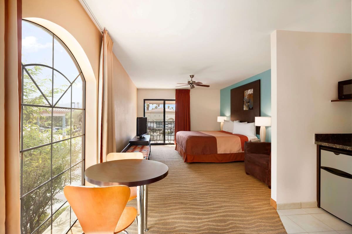 A hotel room with a large window, a bed, a desk with a chair, a television, and a ceiling fan.