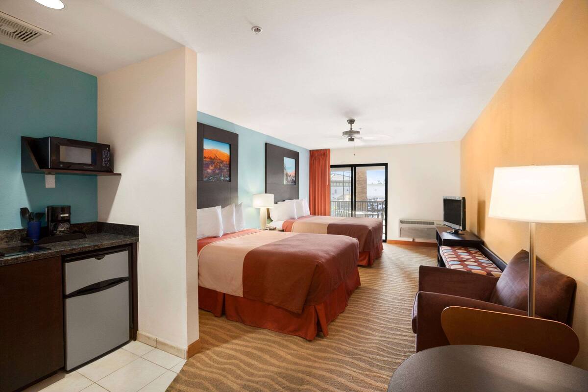 A hotel room with two beds, a desk, a microwave, and a TV.