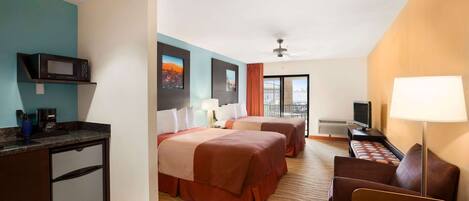 A hotel room with two beds, a desk, a microwave, and a TV.