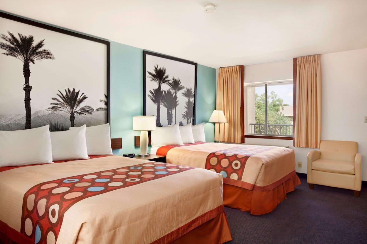 A hotel room with two beds, a chair, a window with curtains, and artwork on the wall.