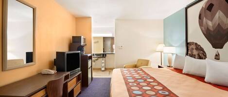 Quarto de hotel com cama, escrivaninha, cadeira, televisão e um espelho grande.