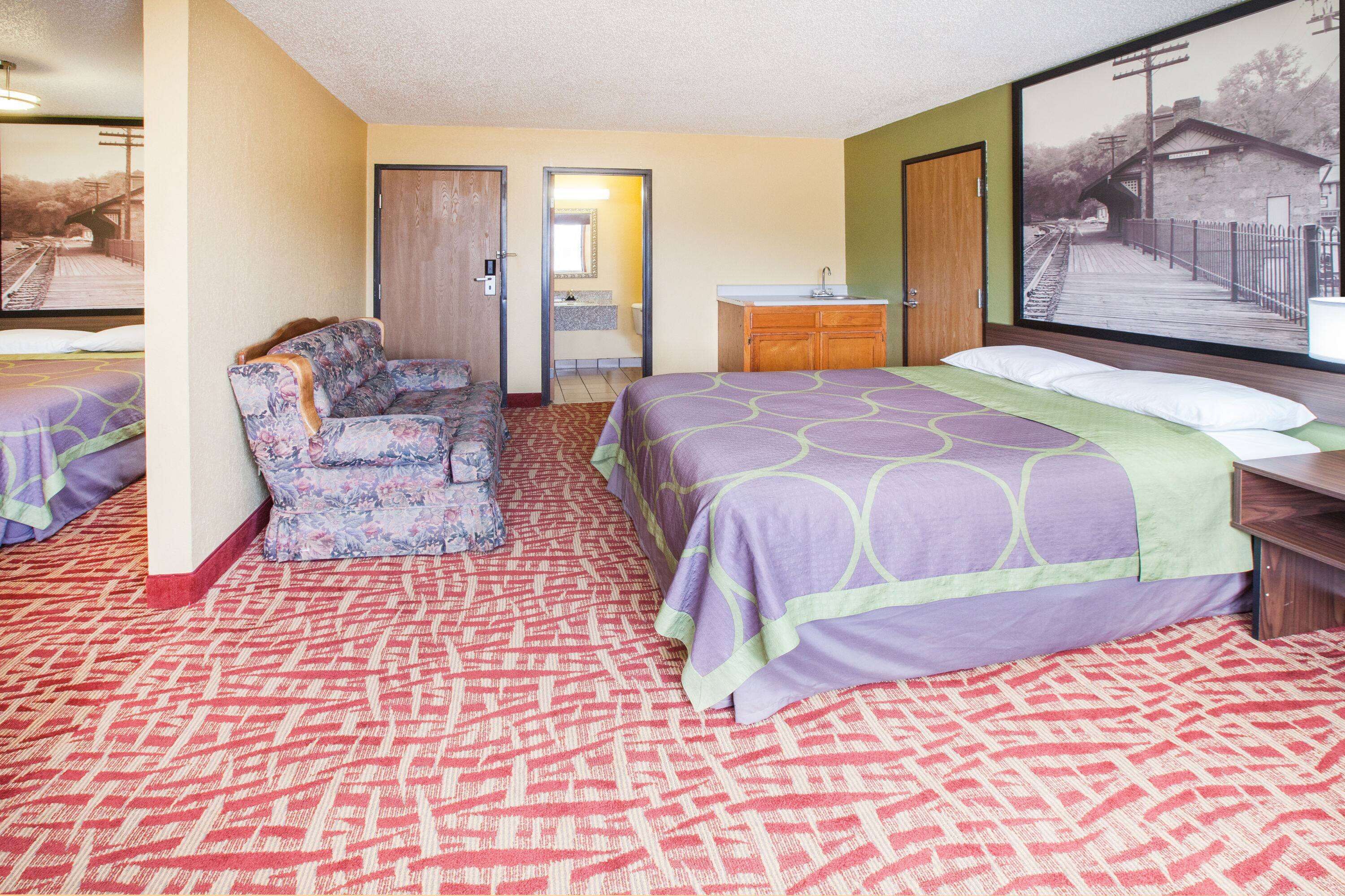 Habitación de hotel con cama, sofá, baño y un amplio ventanal con vistas a un puente.