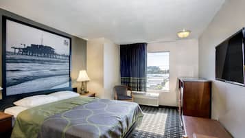 A hotel room with a bed, a desk, a chair, a TV, a window with curtains, and a large picture on the wall.
