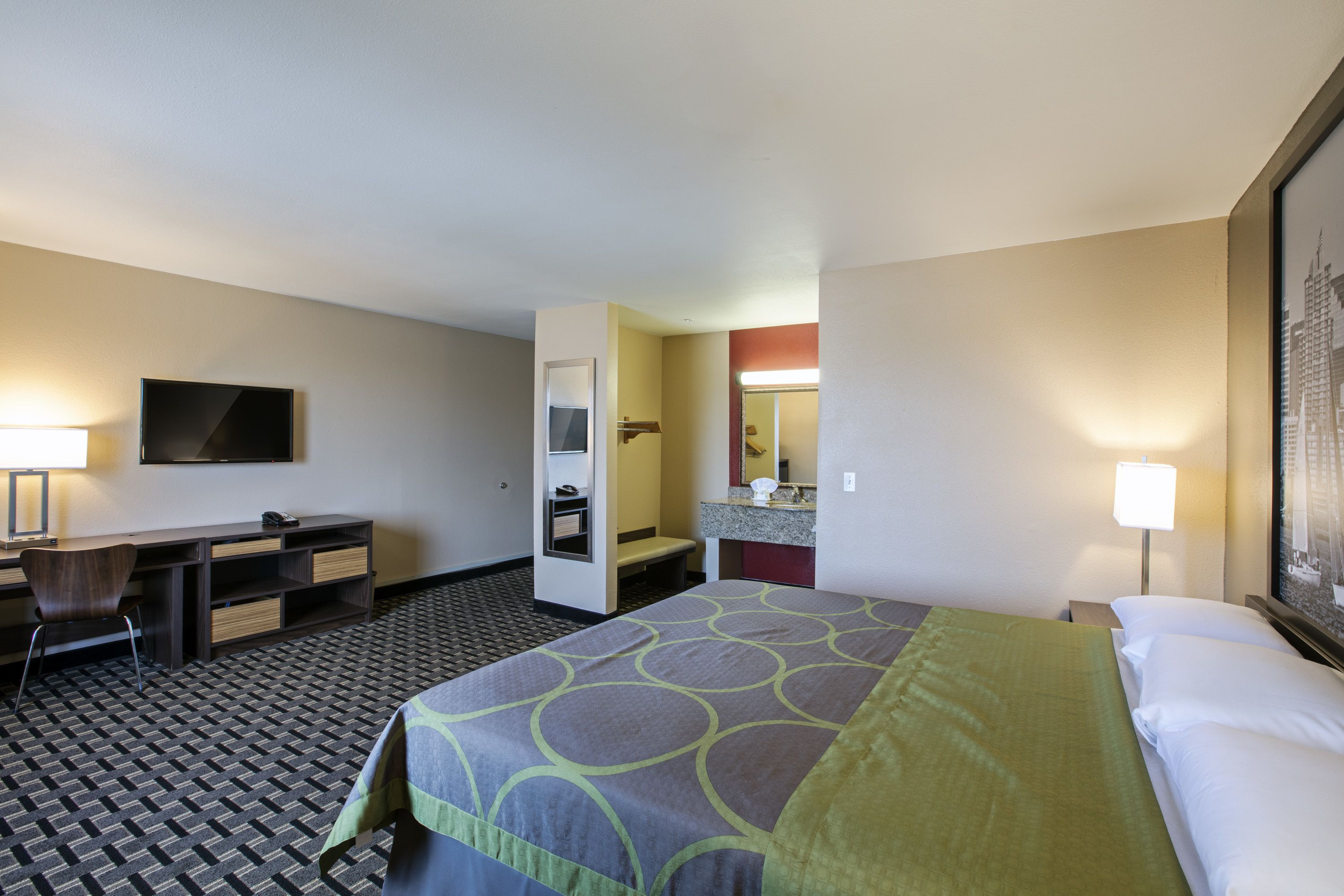 A hotel room with a bed, a desk, a chair, a television, a bathroom, and a mirror.