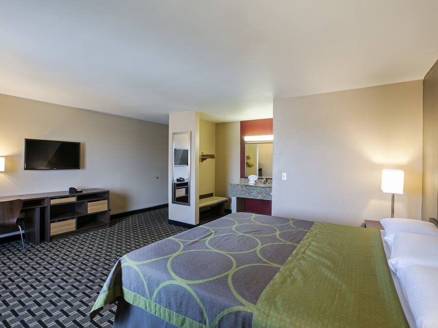 A hotel room with a bed, a desk, a chair, a television, a bathroom, and a mirror.