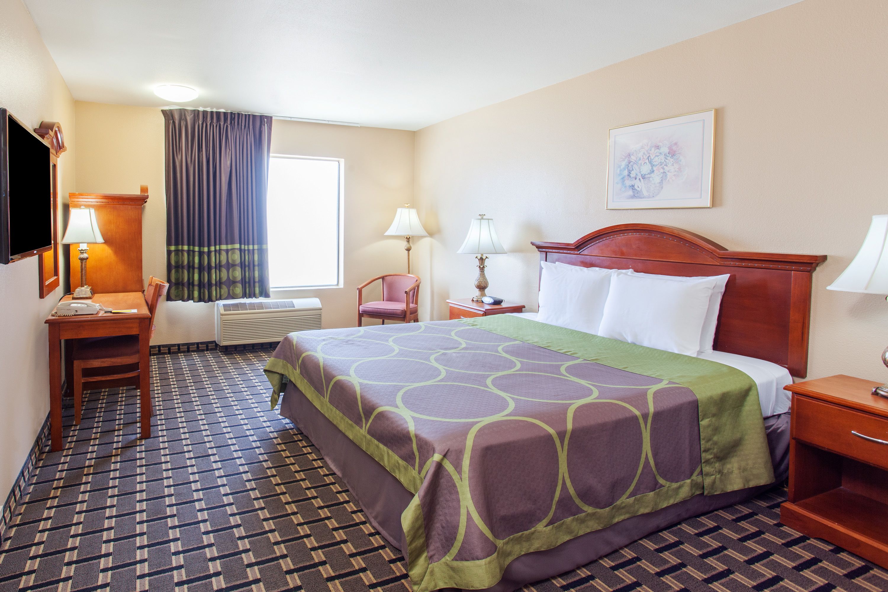 A hotel room with a bed, a desk, a chair, a TV, and a window with curtains.