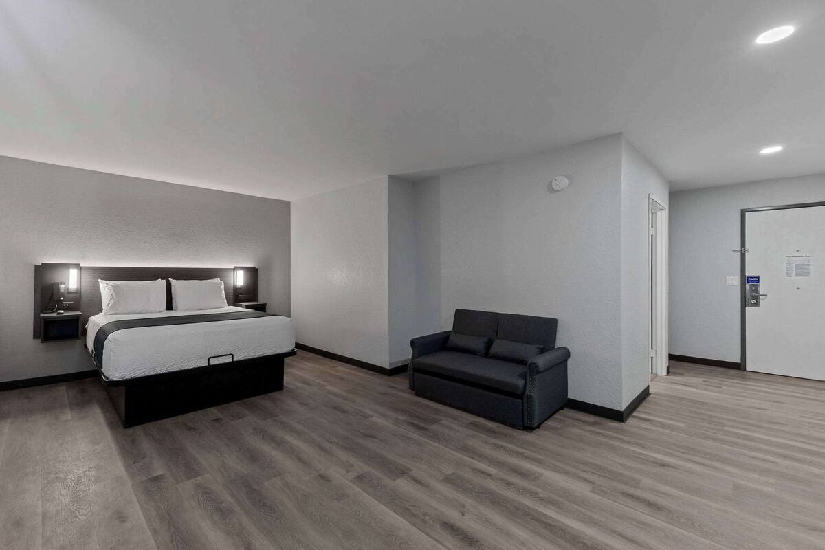 A modern hotel room with a bed, a sofa, and a door.