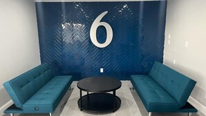Una habitación con dos sofás color turquesa, una mesa redonda negra y una pared azul grande con el número 6.