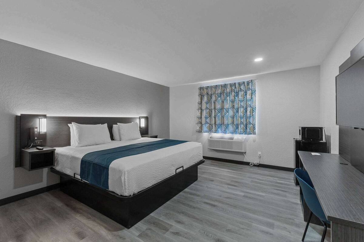A modern hotel room with a bed, bedside tables, a desk, and a television.