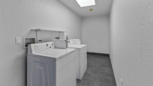 Un lavadero con dos lavadoras y secadoras Whirlpool blancas, un lavabo blanco y una luz en el techo.