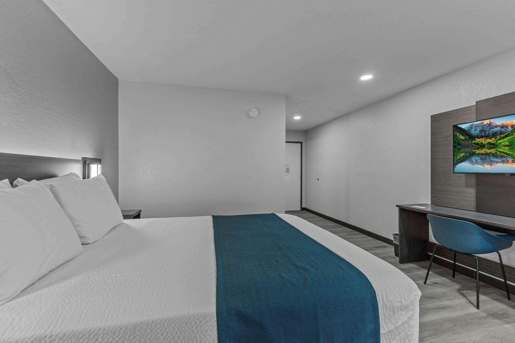 A modern hotel room with a large bed, a desk, and a TV mounted on the wall.