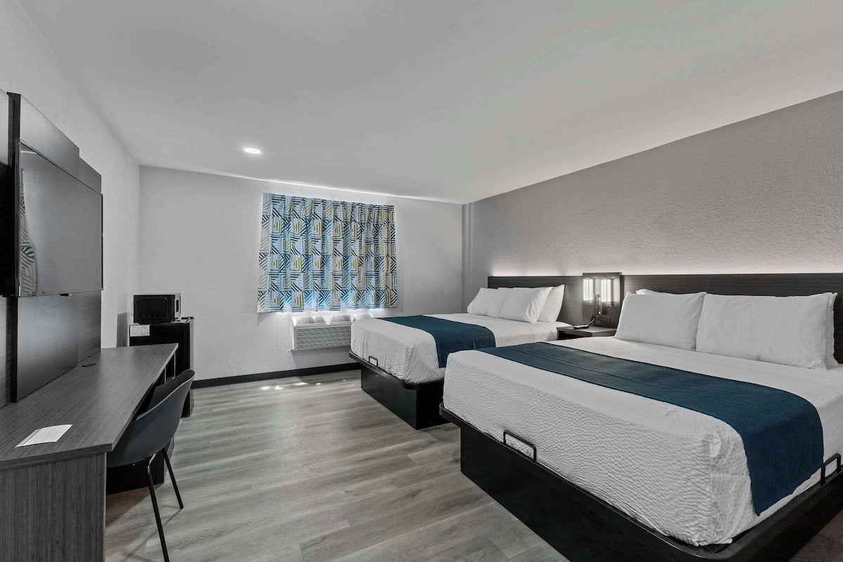 A modern hotel room with two beds, a desk, a TV, and a patterned window.