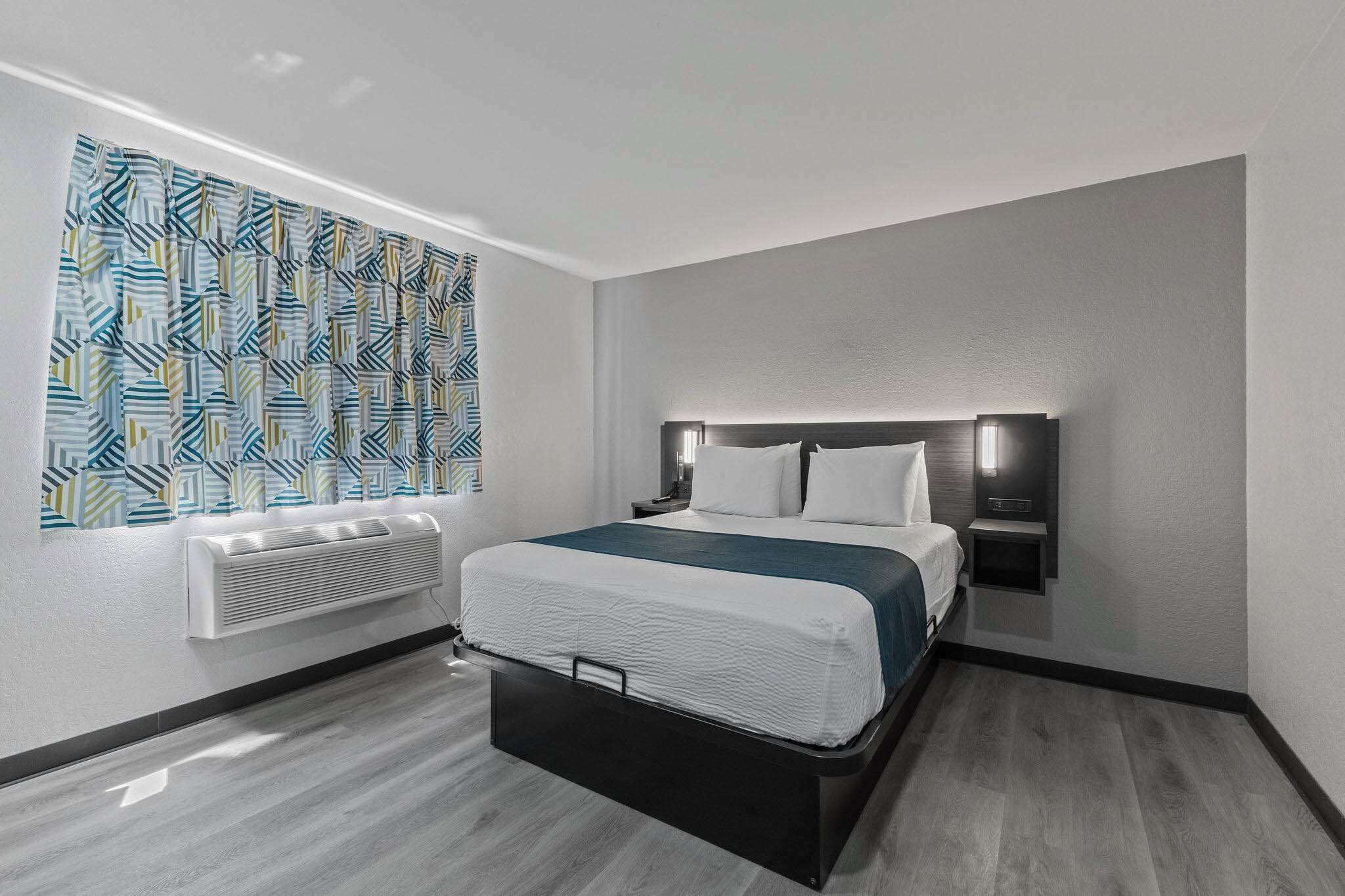 Une chambre d’hôtel moderne, équipée d’un lit, d’un radiateur fixé au mur et d’un rideau à motifs.