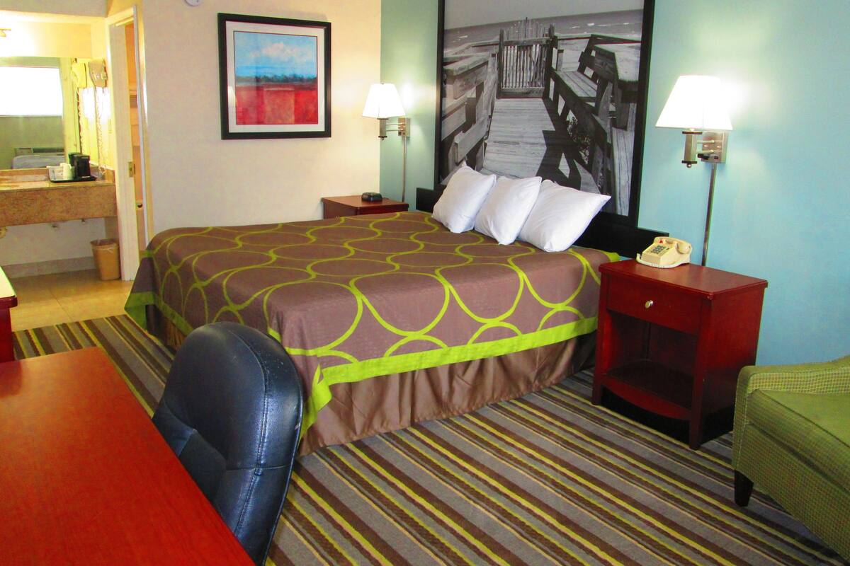 Une chambre d’hôtel avec un grand lit, un bureau, une chaise, un téléphone et un tableau au mur.
