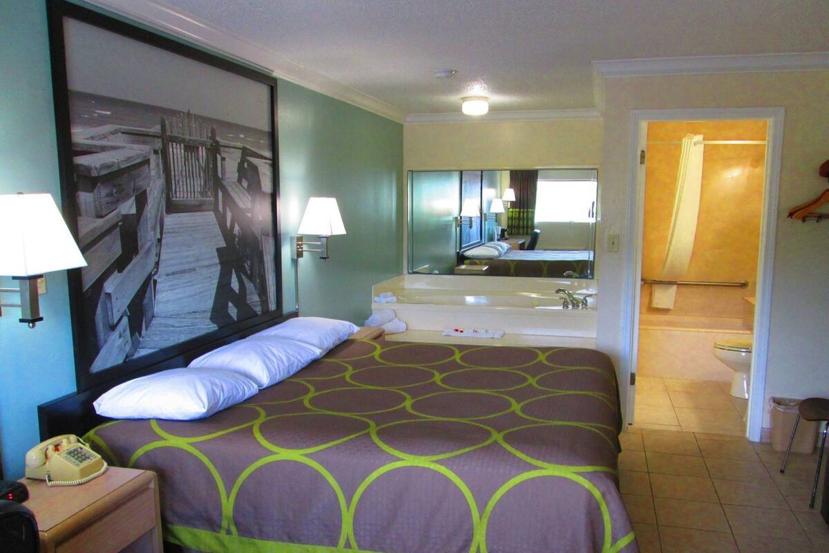 Une chambre d’hôtel comprenant un lit, des lampes de chevet, un téléphone, un grand miroir, une salle de bain avec une baignoire et une douche.